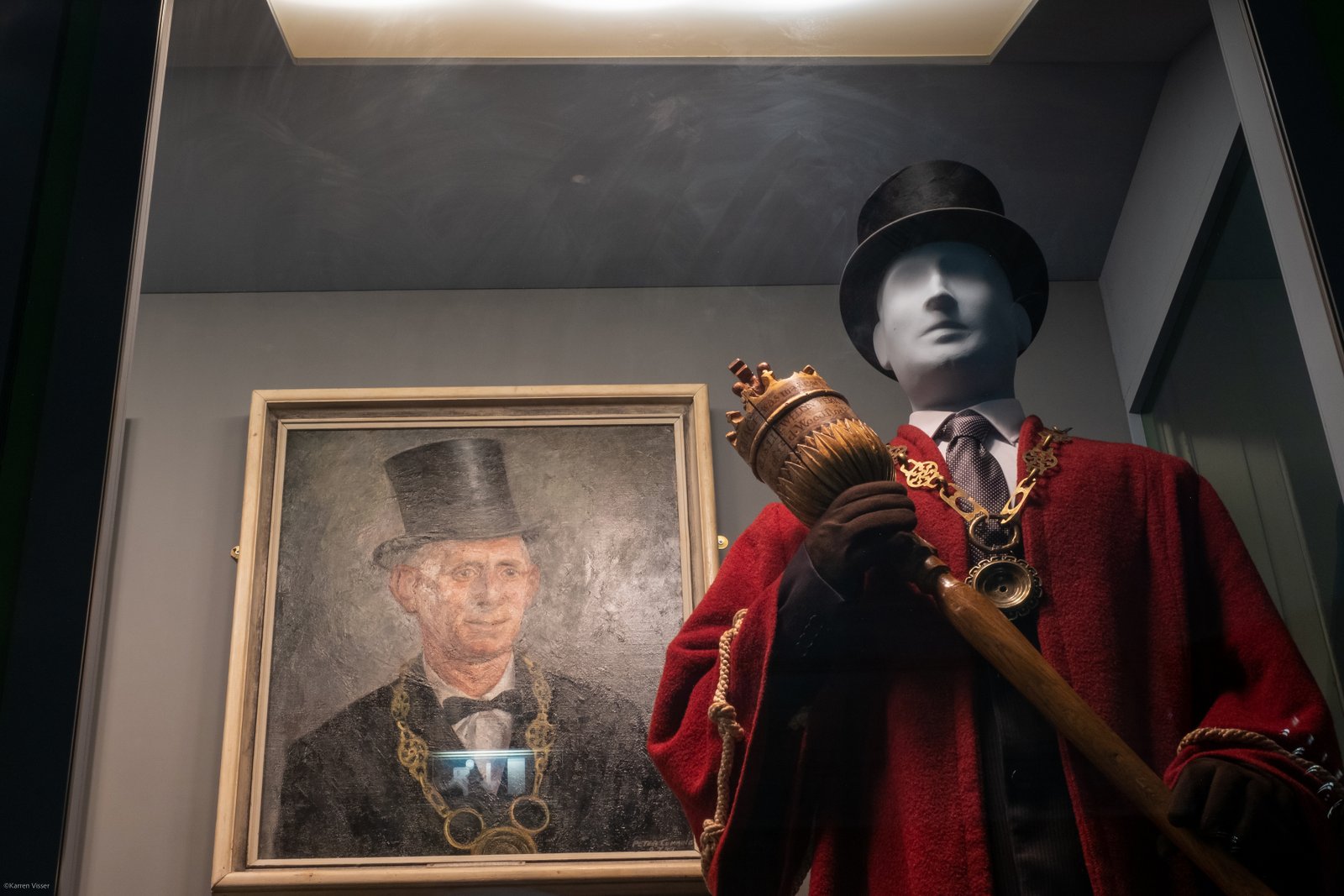 A display case with a mannequin in Mayor’s robes, a top hat and carrying a carved mace seen from the waist up with a portrait of a Mayor in a similar dress.