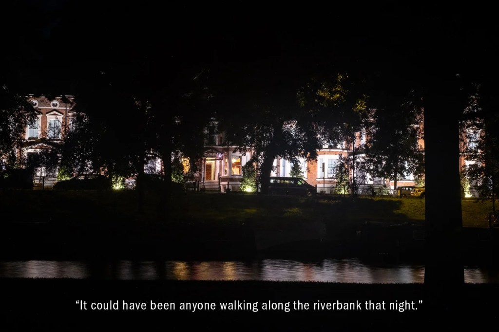 Night scene of river with spot-lit Victorian hotel beyond row of trees and parked cars opposite.