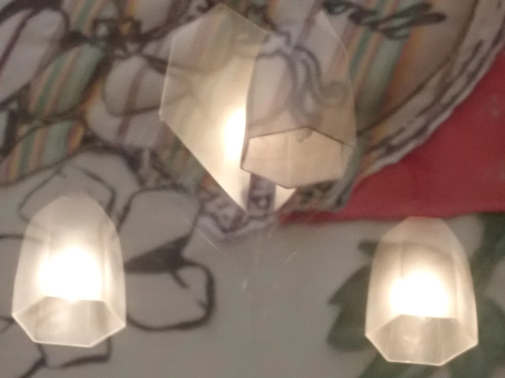 First of four photographs forming a sequence. This one is of a reflection from a hanging light on glass covering embroidered fabric.