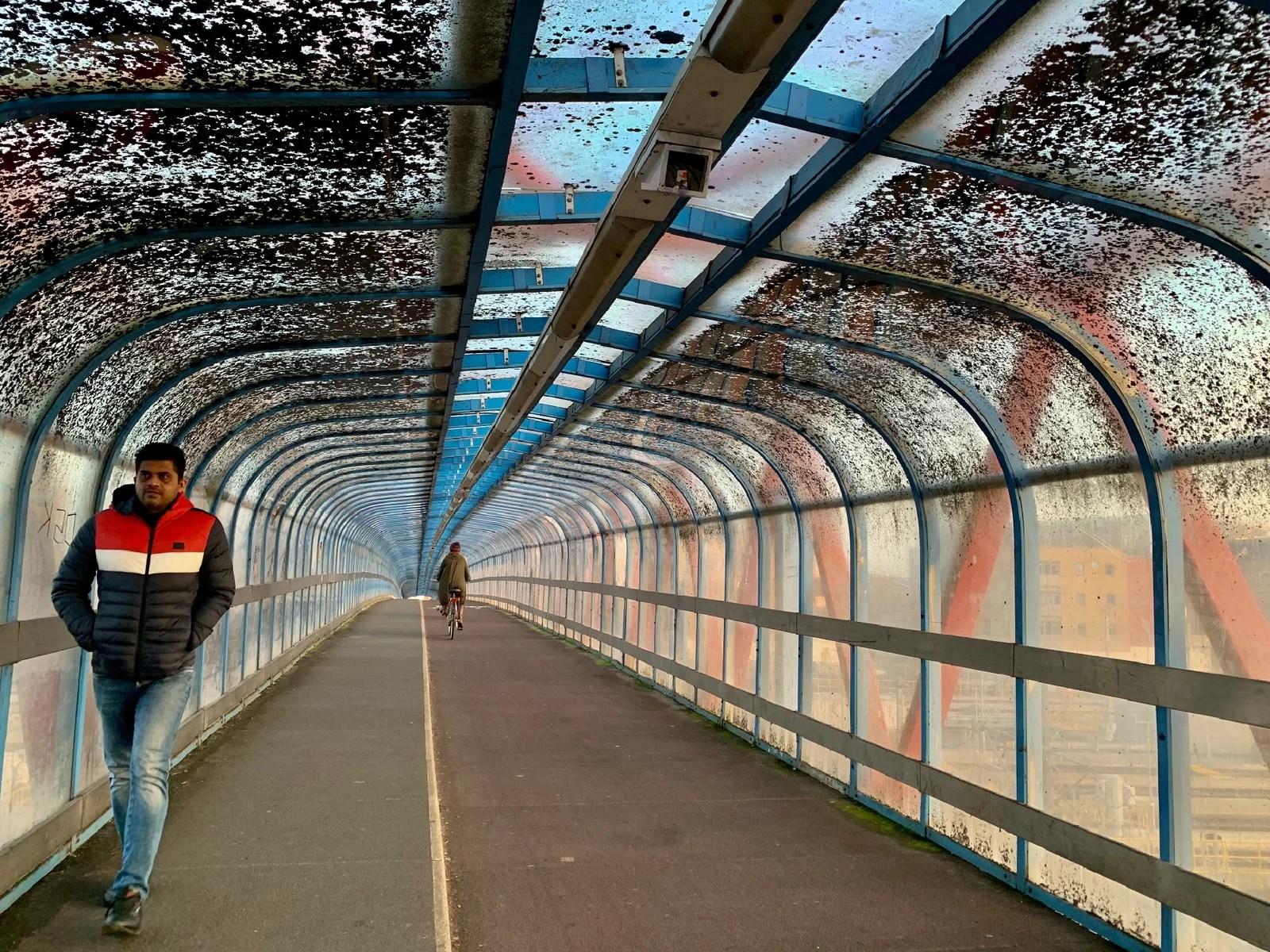 A man crosses a bridge over railway tracks and a cyclist is in the distance.