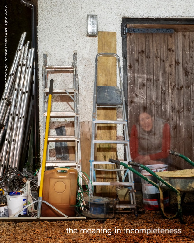 Exterior corner of shed with tools, ladders, and clutter. Faint outline of woman in red top seated on plastic drum, created using light painting photography. Text reads “the meaning in incompleteness.” 
© Karren Visser. Sight Lines, funded by Arts Council England, 2021–22.