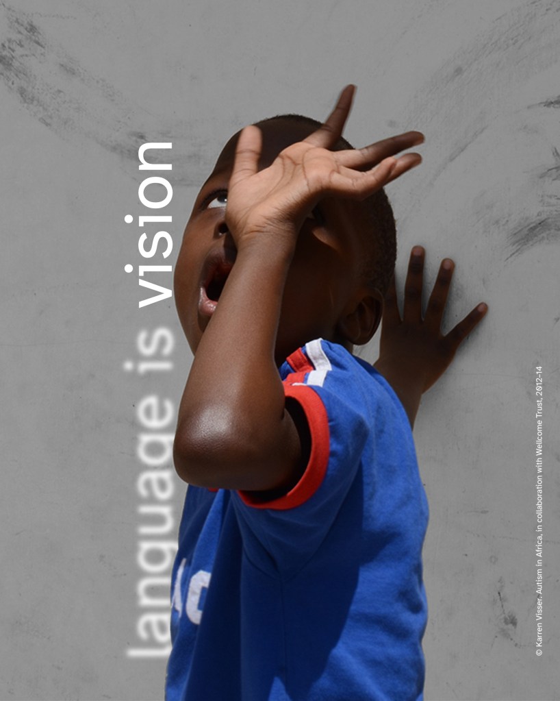 A young child with dark brown skin in a blue T-shirt with red-and-white trim stands against a light grey textured wall, one hand in front of the face, mouth open, white vertical text reads “language is vision.”

© Karren Visser. Autism in Africa, in collaboration with Wellcome Trust, 2012 – 14.